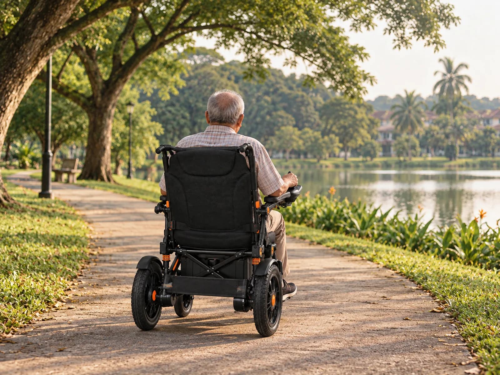 An elderly man seen from behind, driving the electric wheelchair along a paved park path beside a lake, trees on both sides
