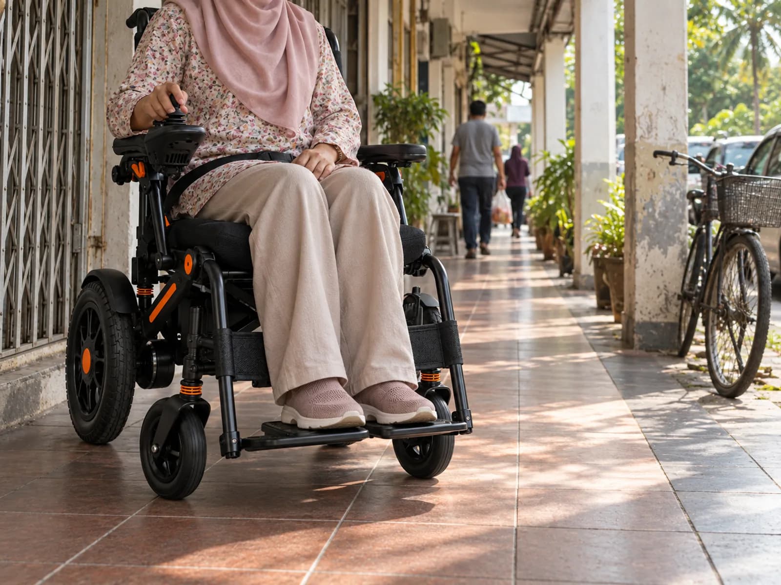 A woman seen from the side, seated in the electric wheelchair on a covered five-foot walkway between shoplot columns