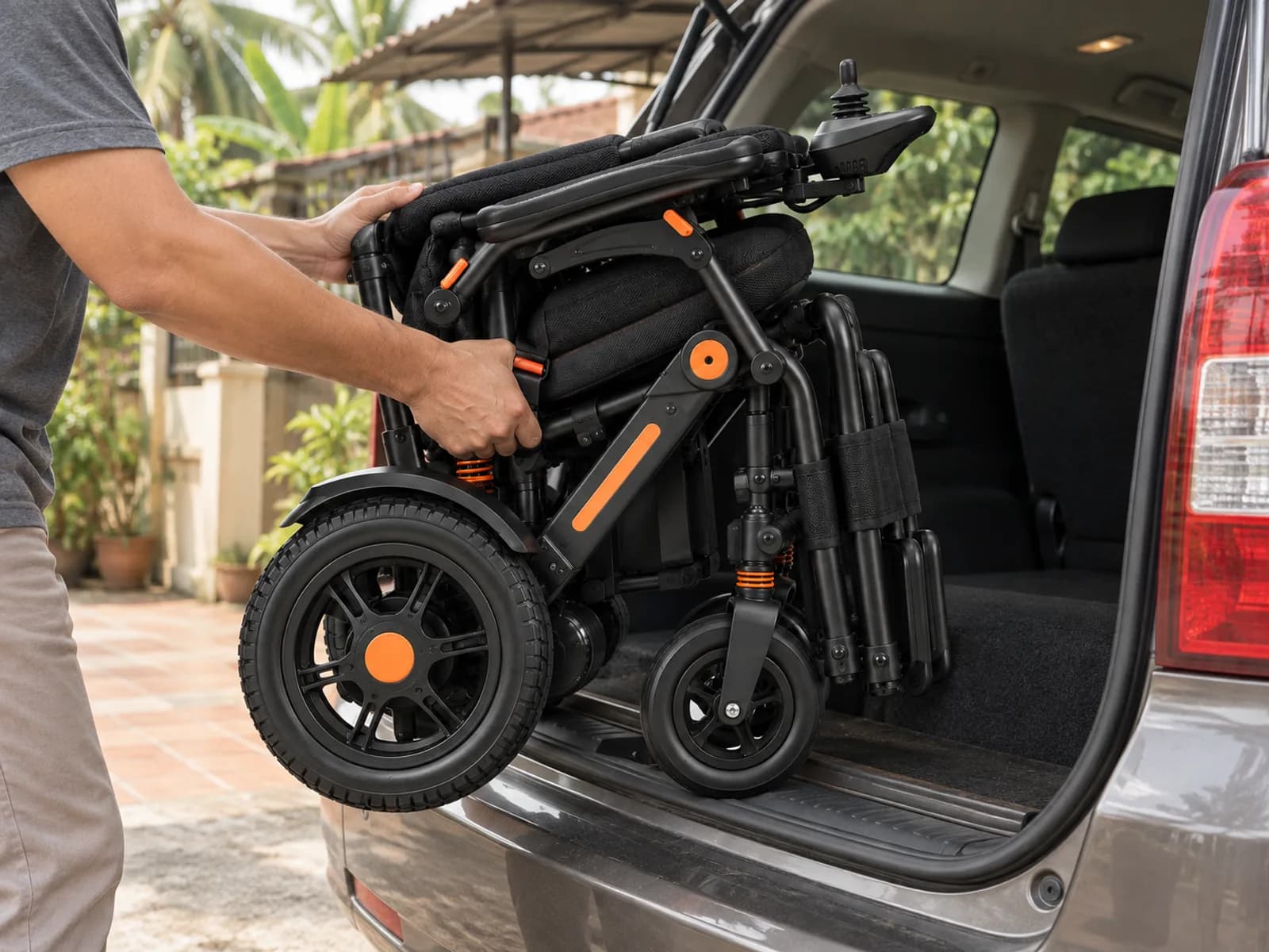 A hand lifting the folded electric wheelchair into the open boot of a car